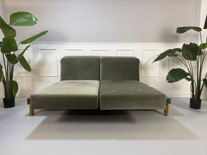 Gebrauchtes grün-graues Stoff Sofa Brühl Modell Moule Large vor einer modernen Wand.