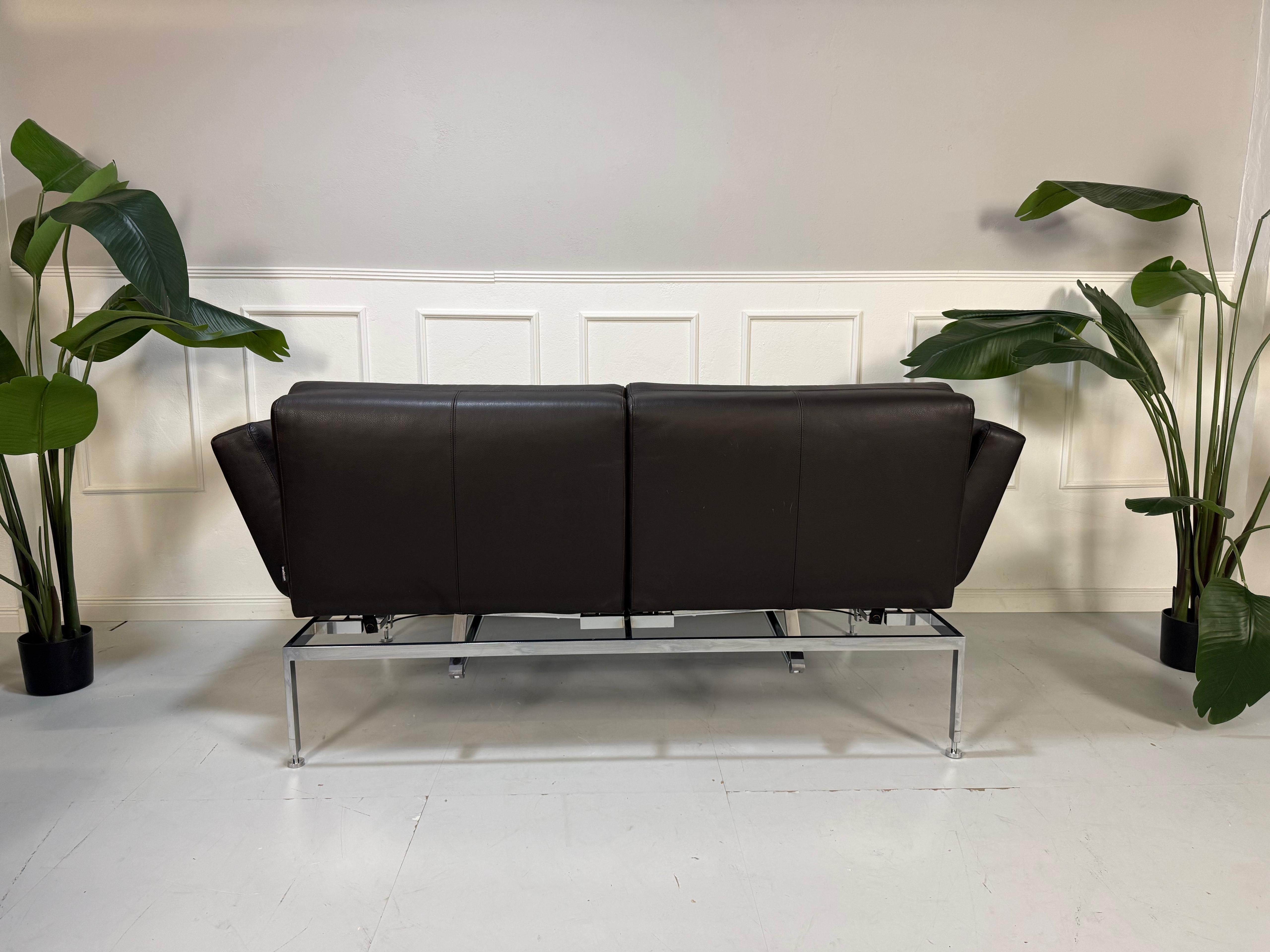 Gebrauchtes braunes Ledersofa Brühl Modell Roro Soft vor einer modernen Wand.