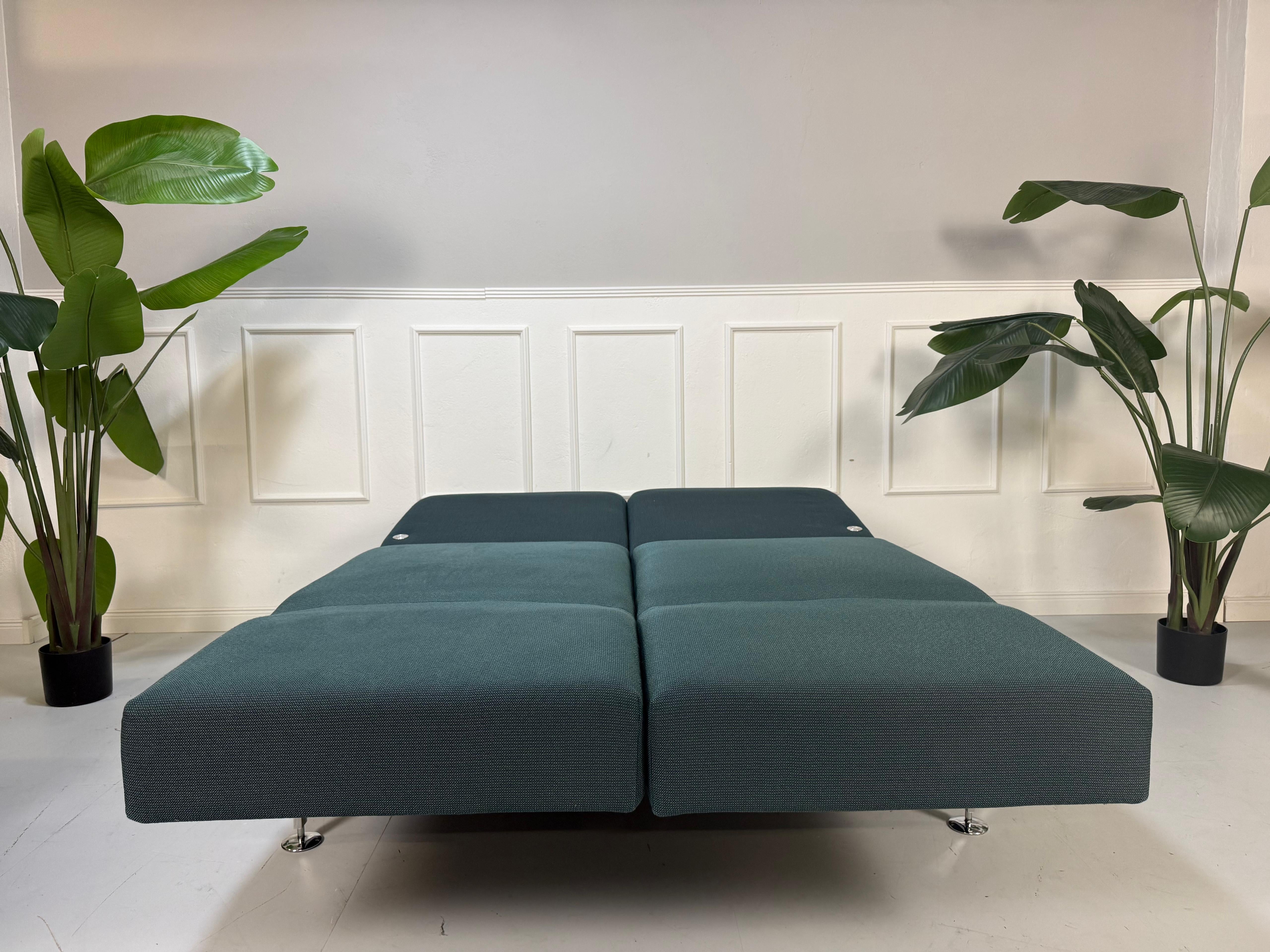 Gebrauchtes blaues Stoff Sofa Brühl Modell Moule Small vor einer modernen Wand.