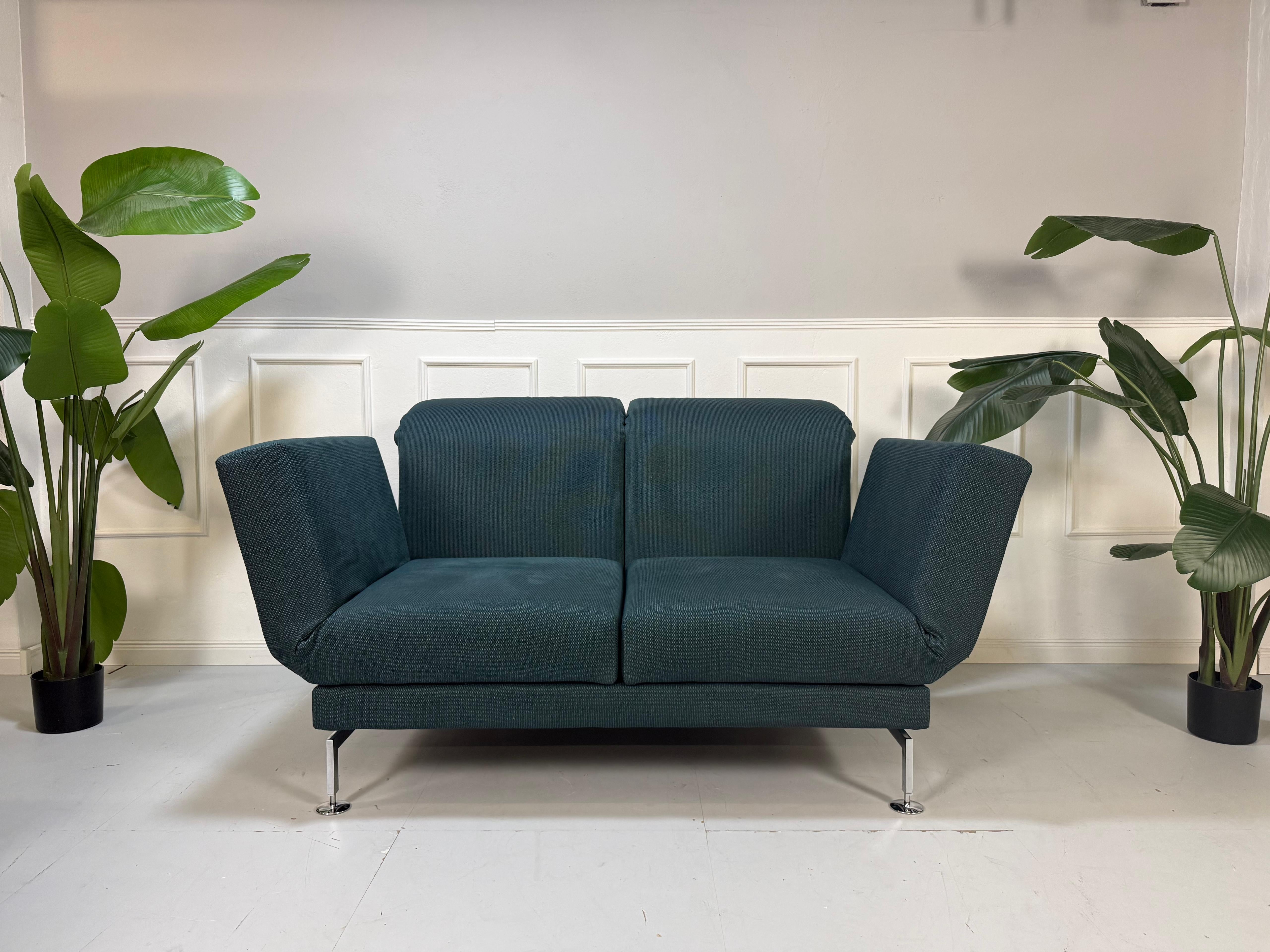 Gebrauchtes blaues Stoff Sofa Brühl Modell Moule Small vor einer modernen Wand.