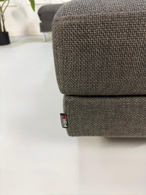Gebrauchtes graues Brühl Fourtwo Designer Stoff Ecksofa vor einer Wand, stilvoll und modern eingerichtet.