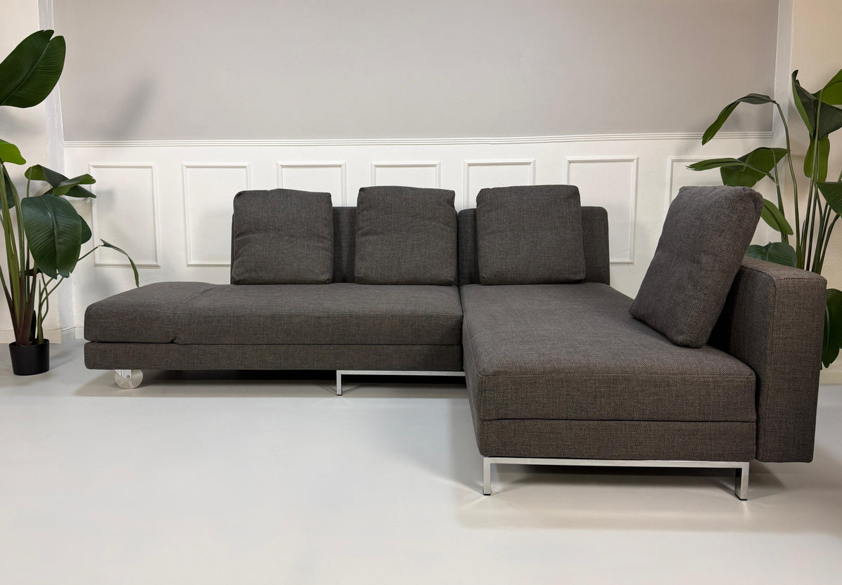 Gebrauchtes graues Brühl Fourtwo Designer Stoff Ecksofa vor einer Wand, stilvoll und modern eingerichtet.
