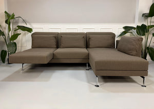 Gebrauchtes braunes Stoff Sofa Brühl Modell Moule vor einer modernen Wand.