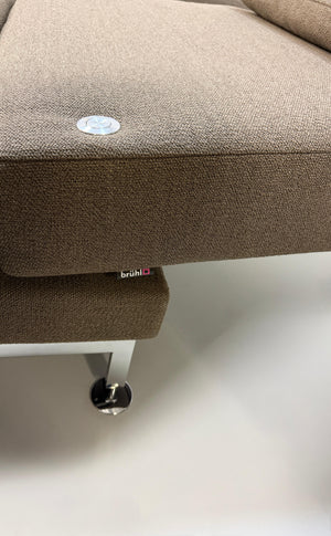 Gebrauchtes braunes Stoff Sofa Brühl Modell Moule vor einer modernen Wand.