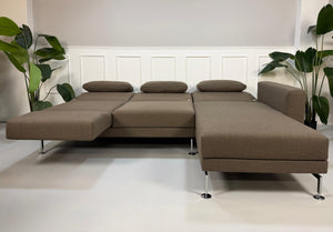 Gebrauchtes braunes Stoff Sofa Brühl Modell Moule vor einer modernen Wand.