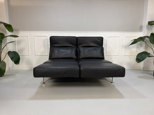 Gebrauchtes schwarzes Ledersofa Brühl Modell Moule vor einer modernen Wand.