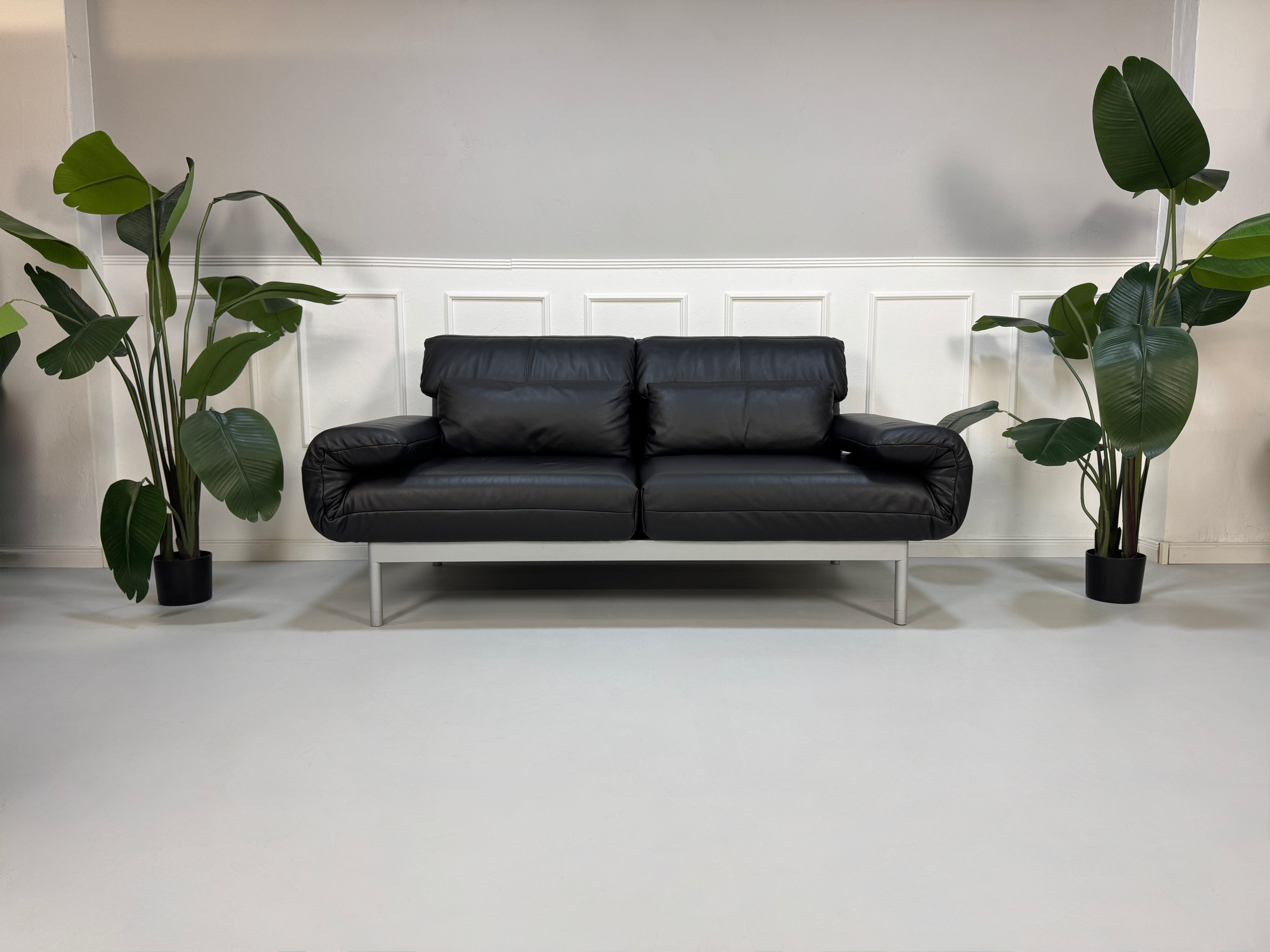Gebrauchtes schwarzes Ledersofa Rolf Benz Modell Plura vor einer modernen Wand.