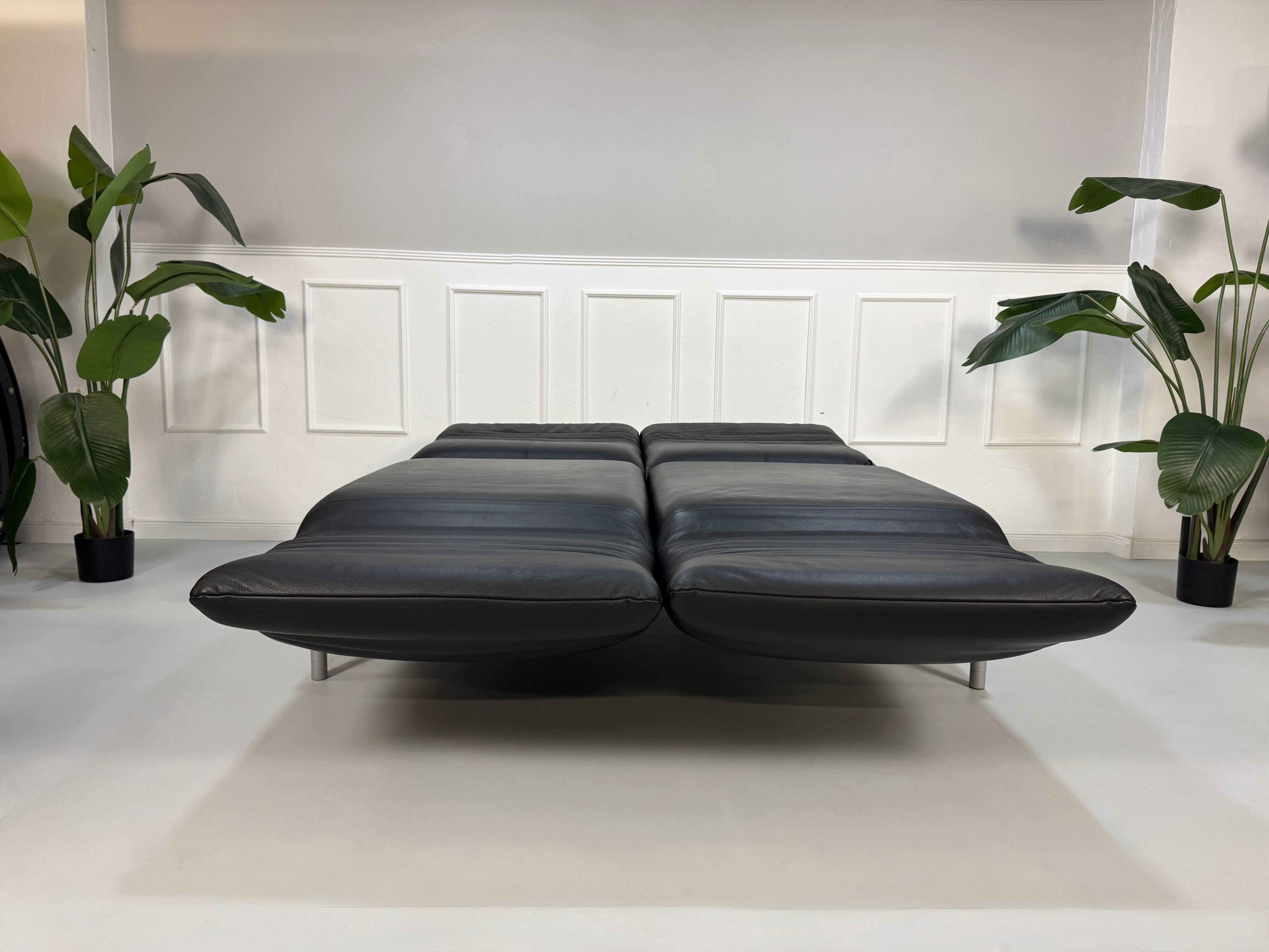 Gebrauchtes schwarzes Ledersofa Rolf Benz Modell Plura vor einer modernen Wand.