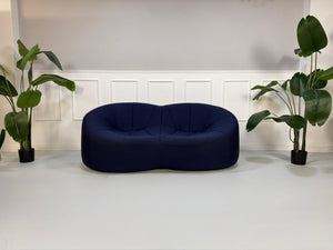 Gebrauchtes blaues Stoff Sofa Ligne Roset Pumpkin vor einer modernen Wand.
