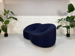 Gebrauchtes blaues Stoff Sofa Ligne Roset Pumpkin vor einer modernen Wand.