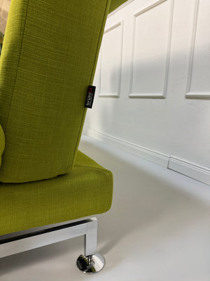 Gebrauchtes grünes Stoff Sofa Brühl Modell Moule vor einer modernen Wand.