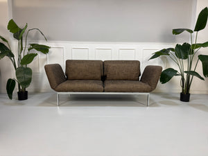 Gebrauchtes braunes Stoff Sofa Brühl Modell Roro vor einer modernen Wand.