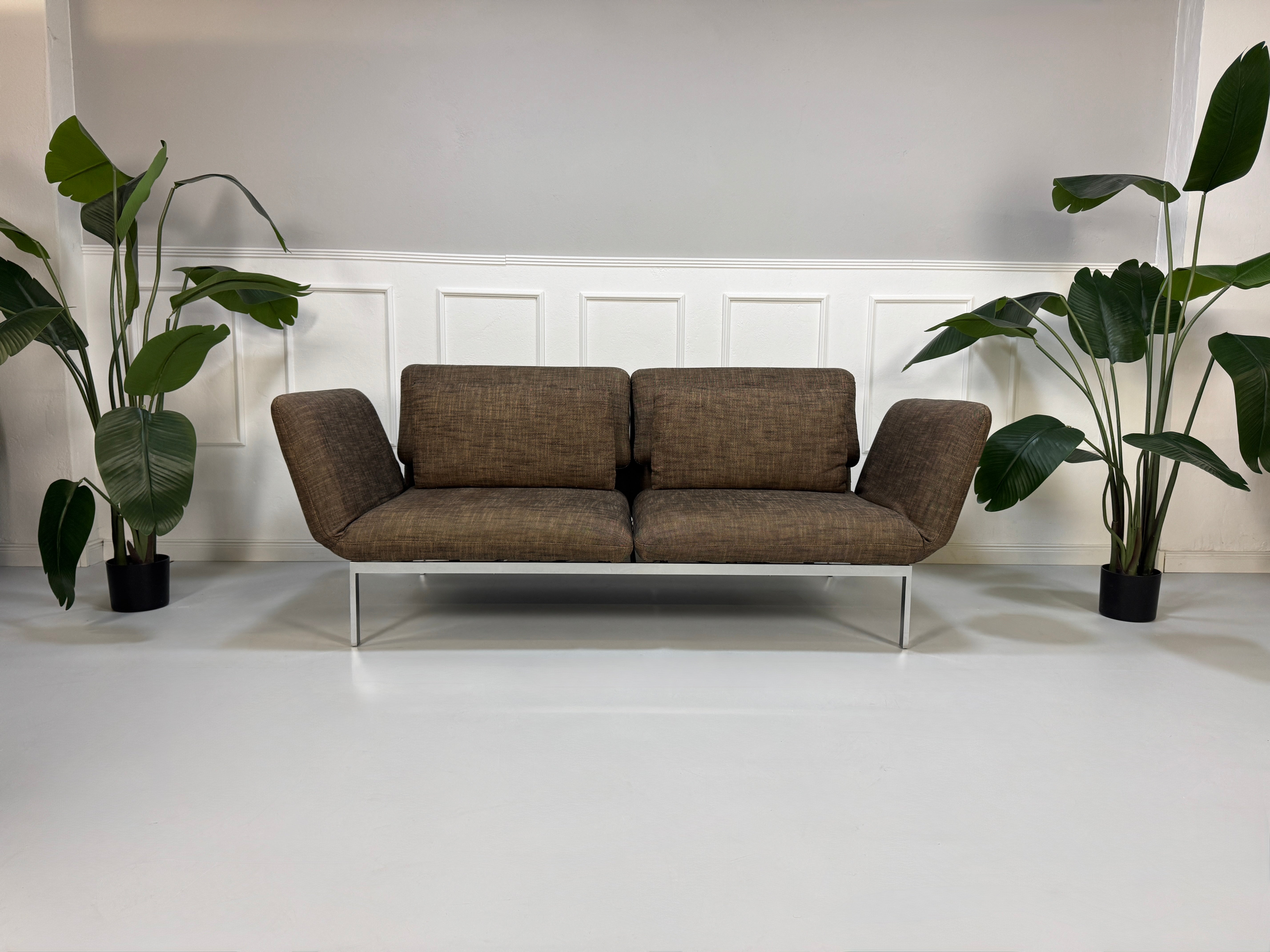 Gebrauchtes braunes Stoff Sofa Brühl Modell Roro vor einer modernen Wand.