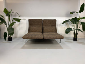 Gebrauchtes braunes Stoff Sofa Brühl Modell Roro vor einer modernen Wand.