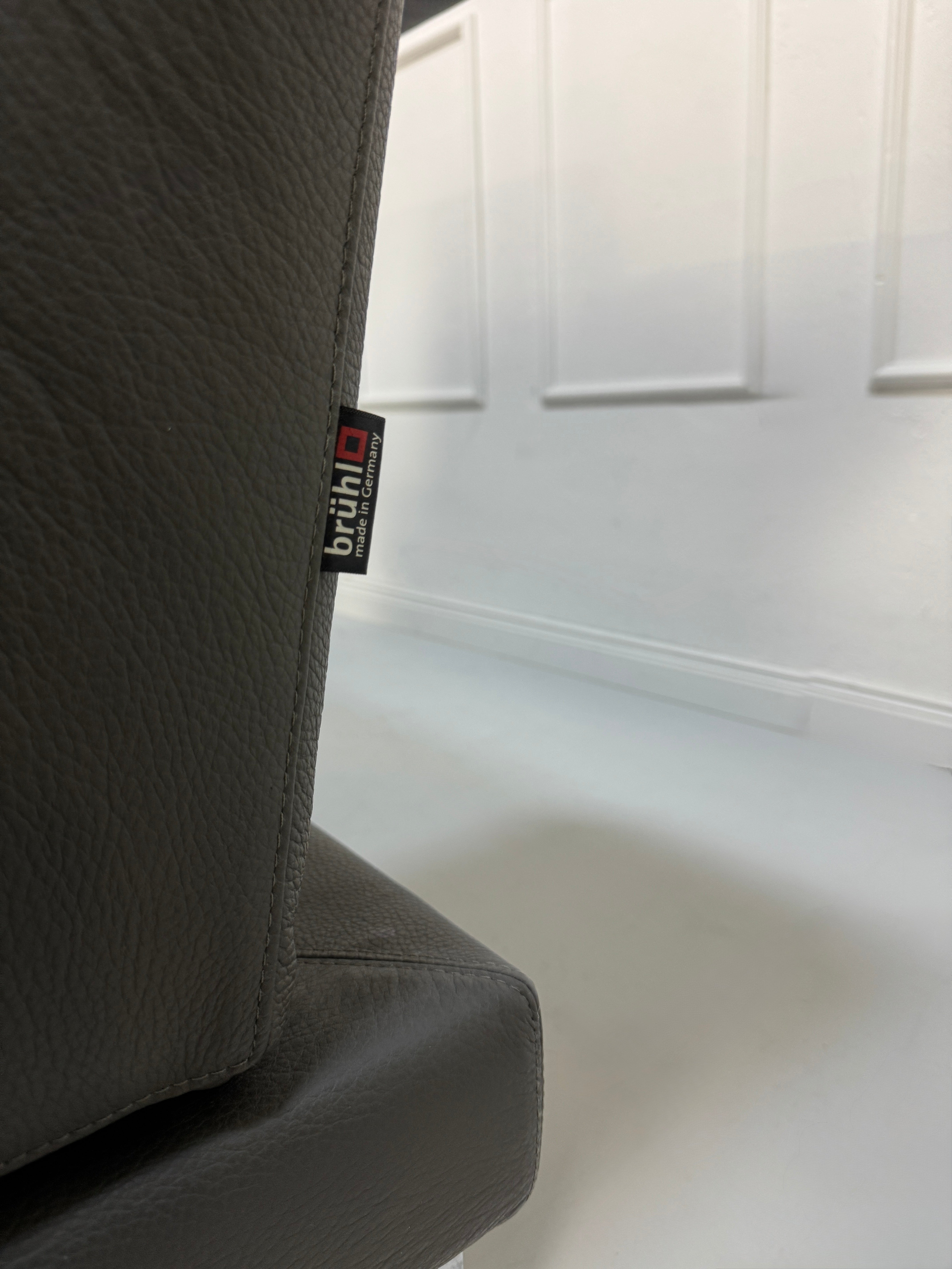 Gebrauchtes graues Brühl Moule Designer Leder Sofa vor einer Wand, stilvoll und modern eingerichtet.