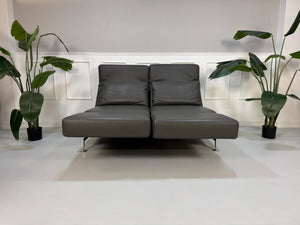 Gebrauchtes graues Brühl Moule Designer Leder Sofa vor einer Wand, stilvoll und modern eingerichtet.