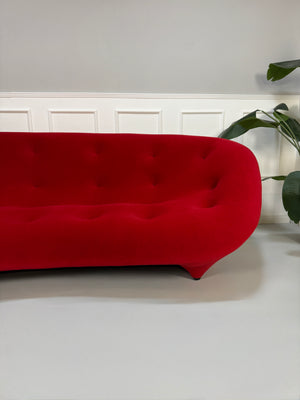 Gebrauchtes rotes Stoff Sofa Ligne Roset Modell Ploum vor einer modernen Wand.