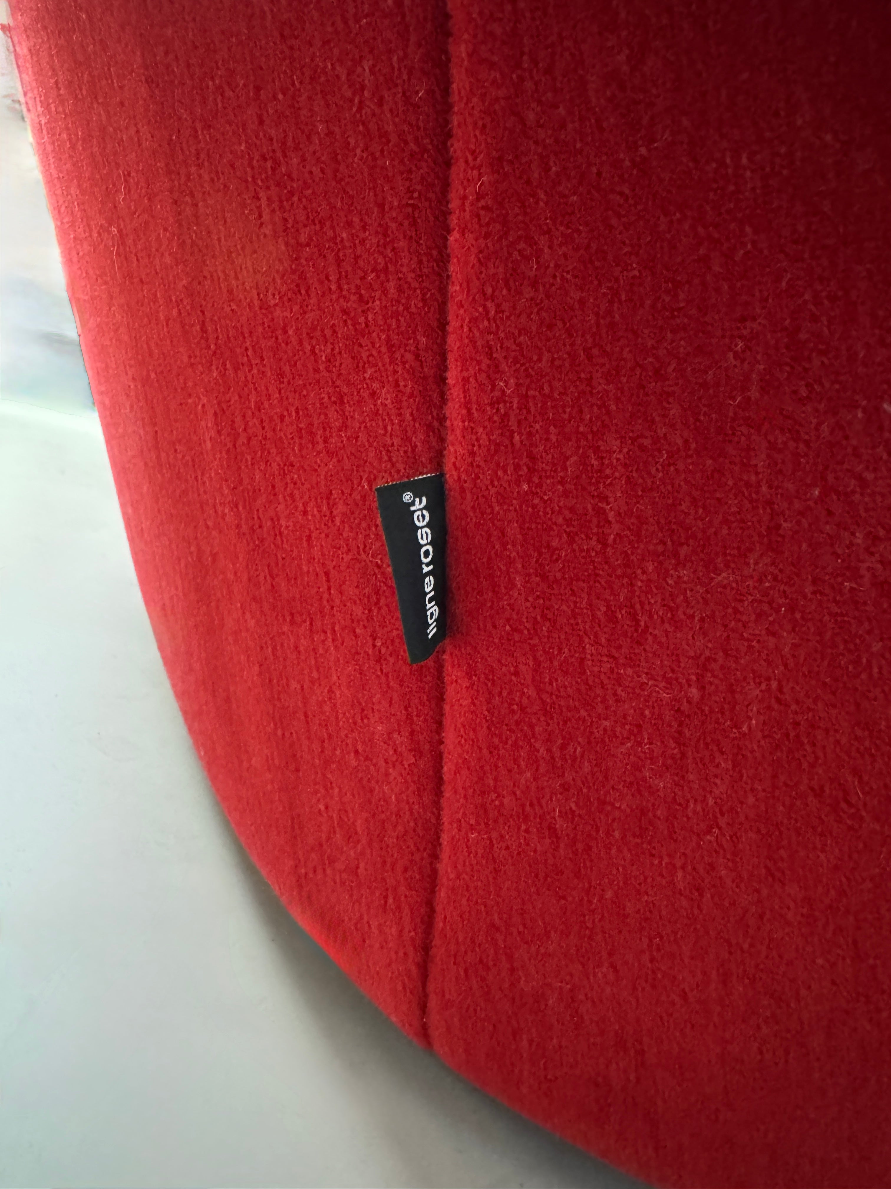 Gebrauchtes rotes Stoff Sofa Ligne Roset Modell Ploum vor einer modernen Wand.