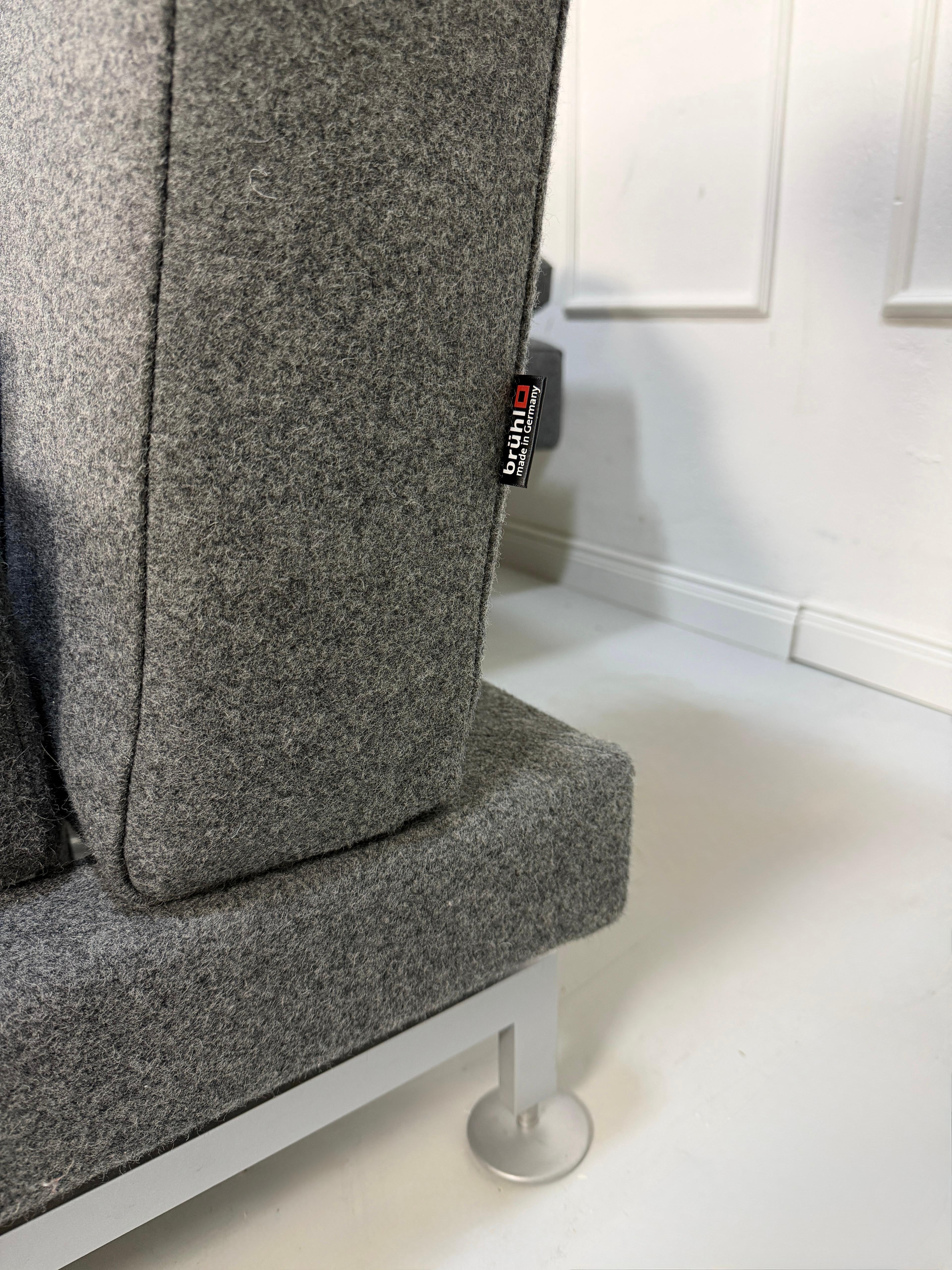 Graues Brühl Moule Ausstellungsstück Designer Stoff Sofa vor einer Wand, stilvoll und modern eingerichtet.