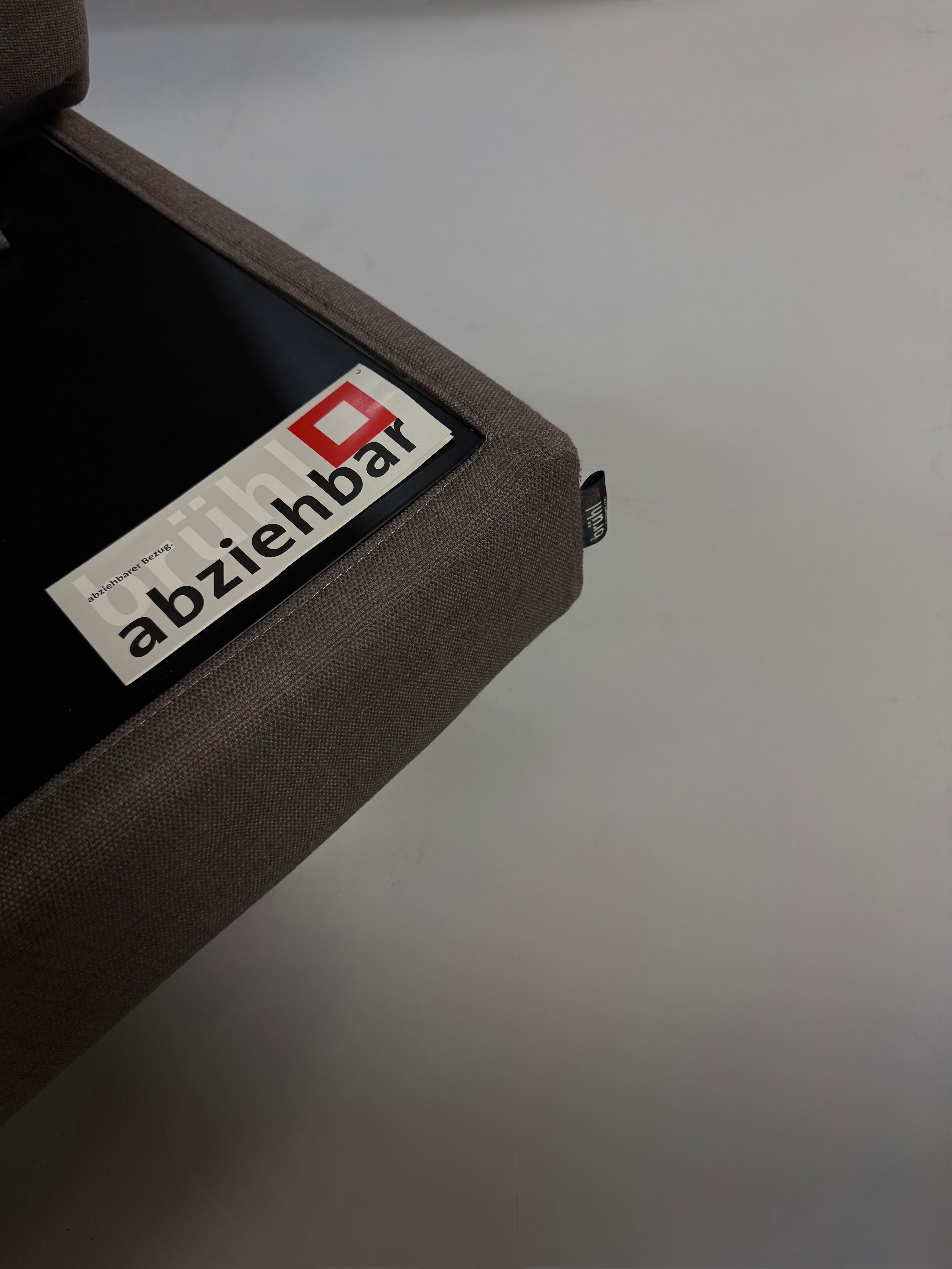 Gebrauchtes graues Brühl Four Two Designer Stoff Sofa vor einer Wand, stilvoll und modern eingerichtet.