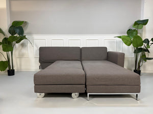 Gebrauchtes graues Brühl Four Two Designer Stoff Sofa vor einer Wand, stilvoll und modern eingerichtet.