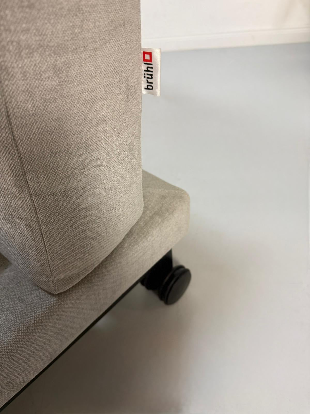 Gebrauchtes graues Brühl Moule Designer Stoff Sofa vor einer Wand, stilvoll und modern eingerichtet.