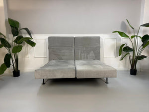 Gebrauchtes graues Brühl Moule Designer Stoff Sofa vor einer Wand, stilvoll und modern eingerichtet.
