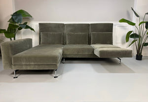 Gebrauchtes grau grünes Brühl Moule Designer Stoff Sofa vor einer Wand, stilvoll und modern eingerichtet.