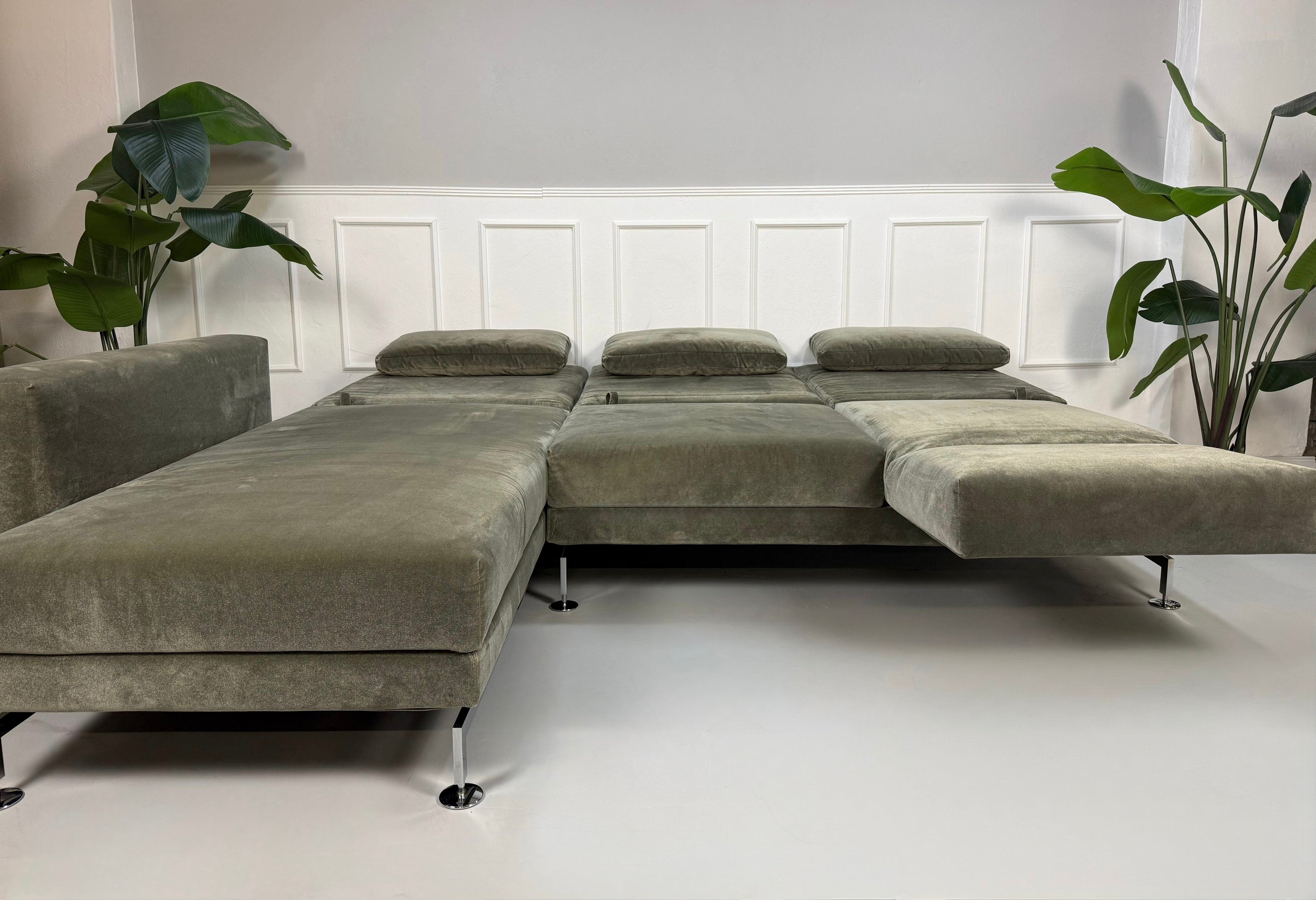 Gebrauchtes grau grünes Brühl Moule Designer Stoff Sofa vor einer Wand, stilvoll und modern eingerichtet.