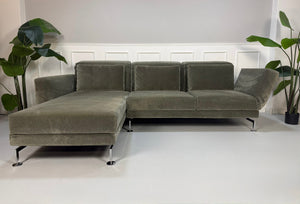 Gebrauchtes grau grünes Brühl Moule Designer Stoff Sofa vor einer Wand, stilvoll und modern eingerichtet.