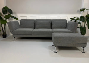 Gebrauchtes graues Brühl Moule Designer Stoff Sofa mit Hocker vor einer Wand, stilvoll und modern eingerichtet.