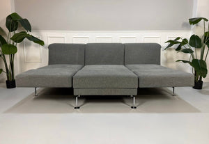 Gebrauchtes graues Brühl Moule Designer Stoff Sofa mit Hocker vor einer Wand, stilvoll und modern eingerichtet.