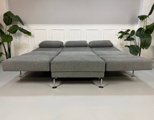 Gebrauchtes graues Brühl Moule Designer Stoff Sofa mit Hocker vor einer Wand, stilvoll und modern eingerichtet.