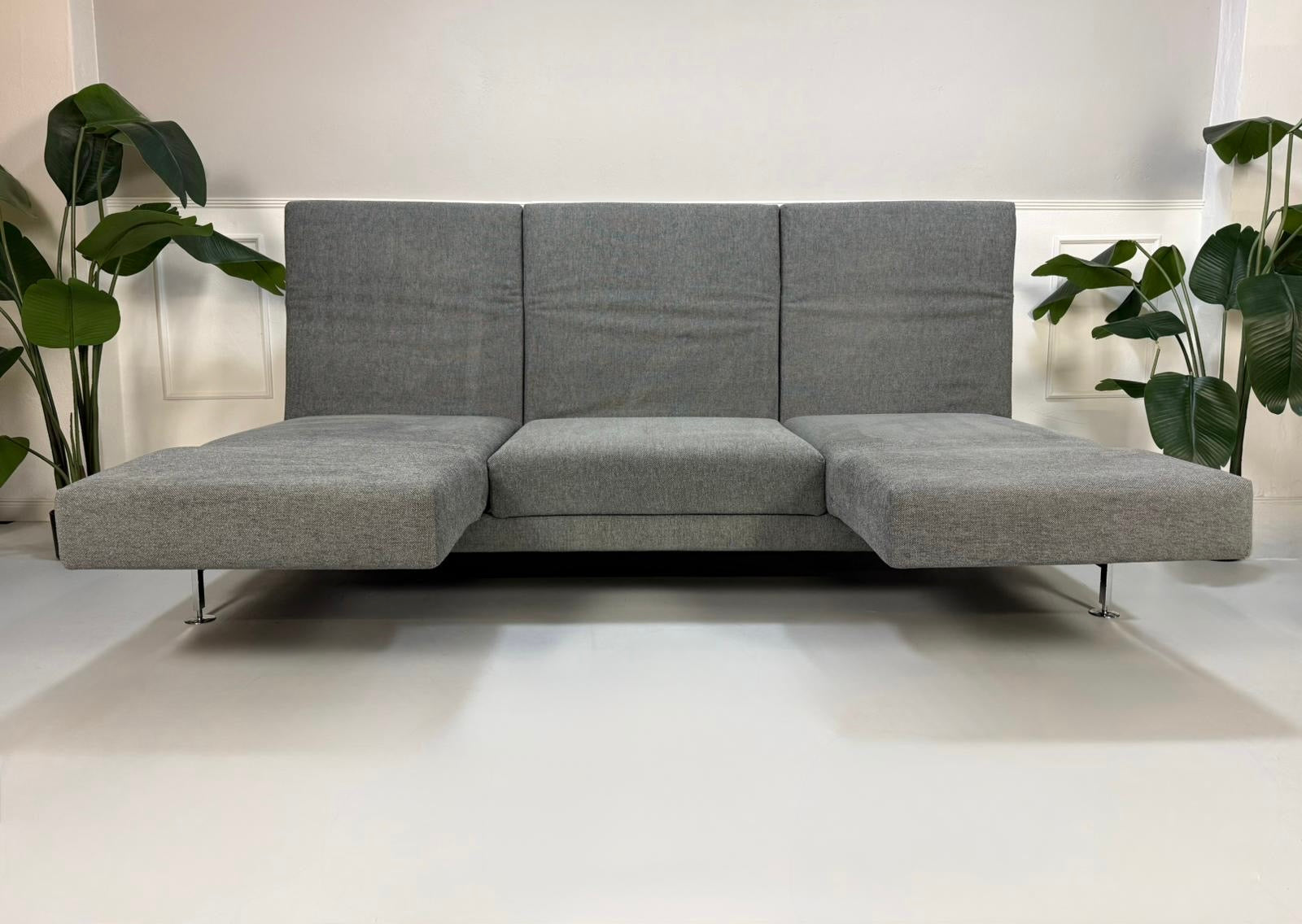 Gebrauchtes graues Brühl Moule Designer Stoff Sofa mit Hocker vor einer Wand, stilvoll und modern eingerichtet.