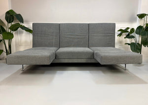 Gebrauchtes graues Brühl Moule Designer Stoff Sofa mit Hocker vor einer Wand, stilvoll und modern eingerichtet.