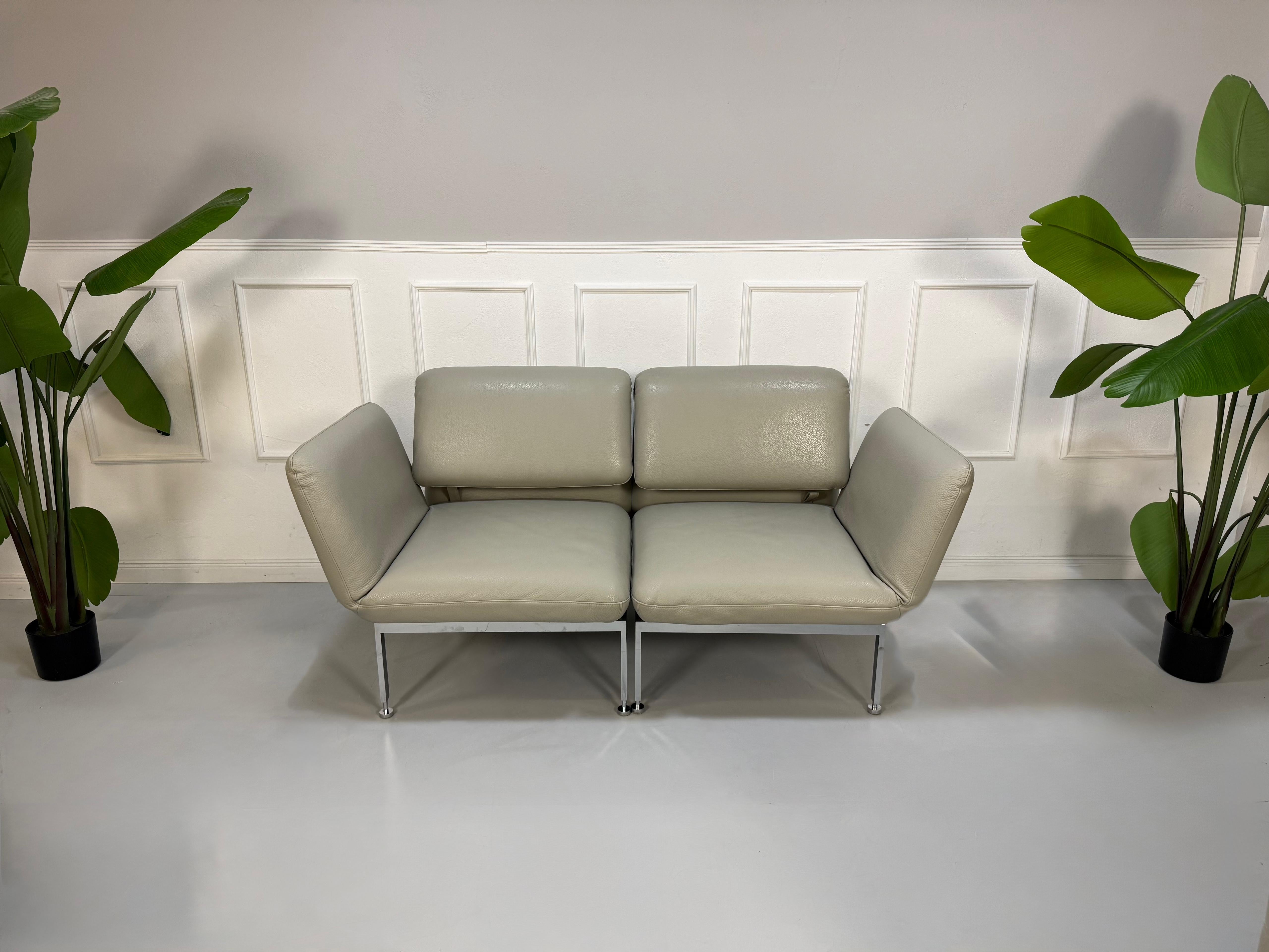 Gebrauchtes graues Brühl Roro Designer Leder Sofa vor einer Wand, stilvoll und modern eingerichtet.