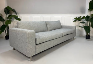 Refurbished graues Bolia Scandinavia Designer Stoff Sofa mit Hocker vor einer Wand, stilvoll und modern eingerichtet.