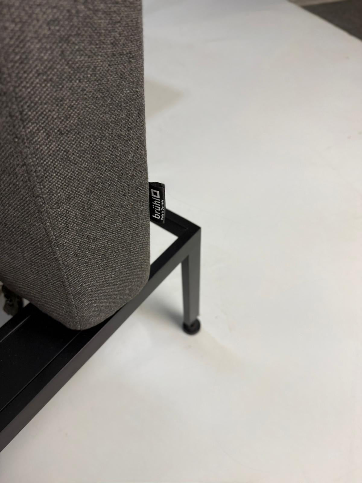 Gebrauchtes graues Brühl Roro Soft Designer Stoff Sofa vor einer Wand, stilvoll und modern eingerichtet.