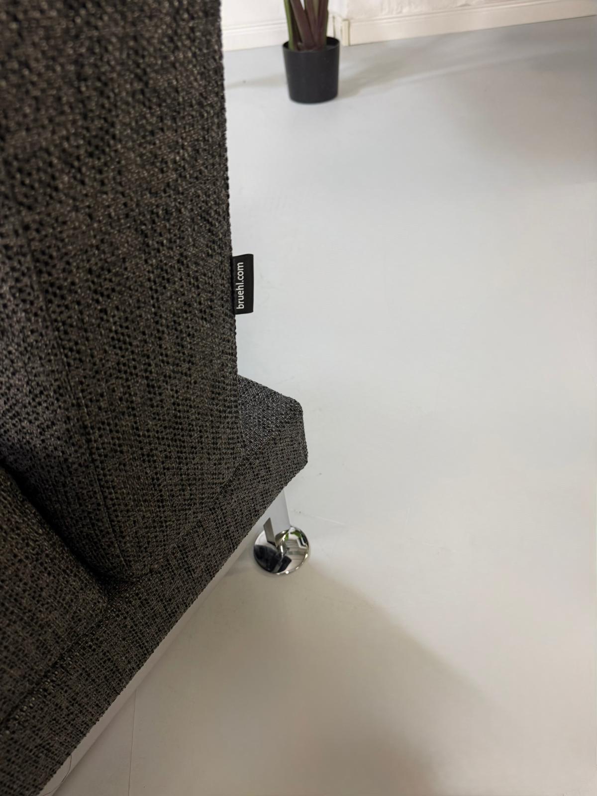 Gebrauchtes graues Brühl Moule Designer Stoff Sofa vor einer Wand, stilvoll und modern eingerichtet.