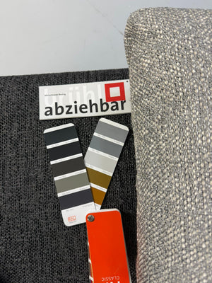 Gebrauchtes graues Brühl Moule Designer Stoff Sofa vor einer Wand, stilvoll und modern eingerichtet.