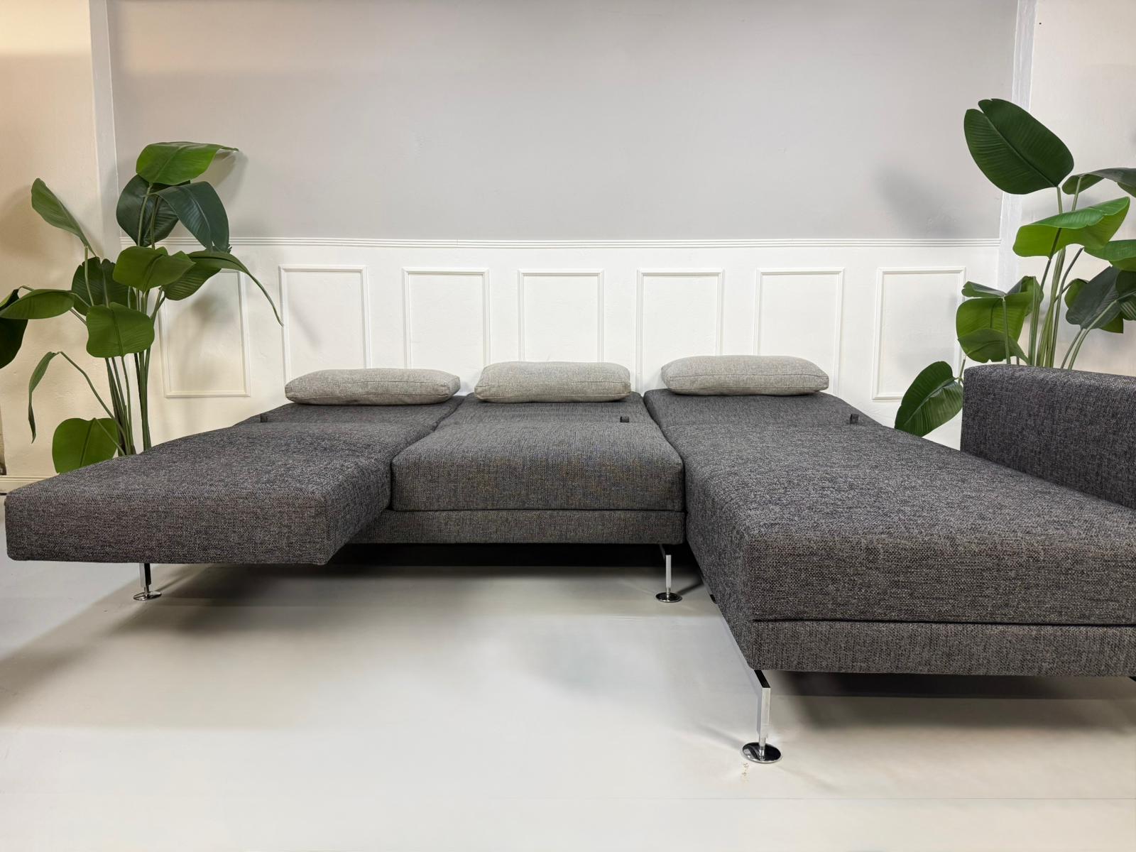 Gebrauchtes graues Brühl Moule Designer Stoff Sofa vor einer Wand, stilvoll und modern eingerichtet.