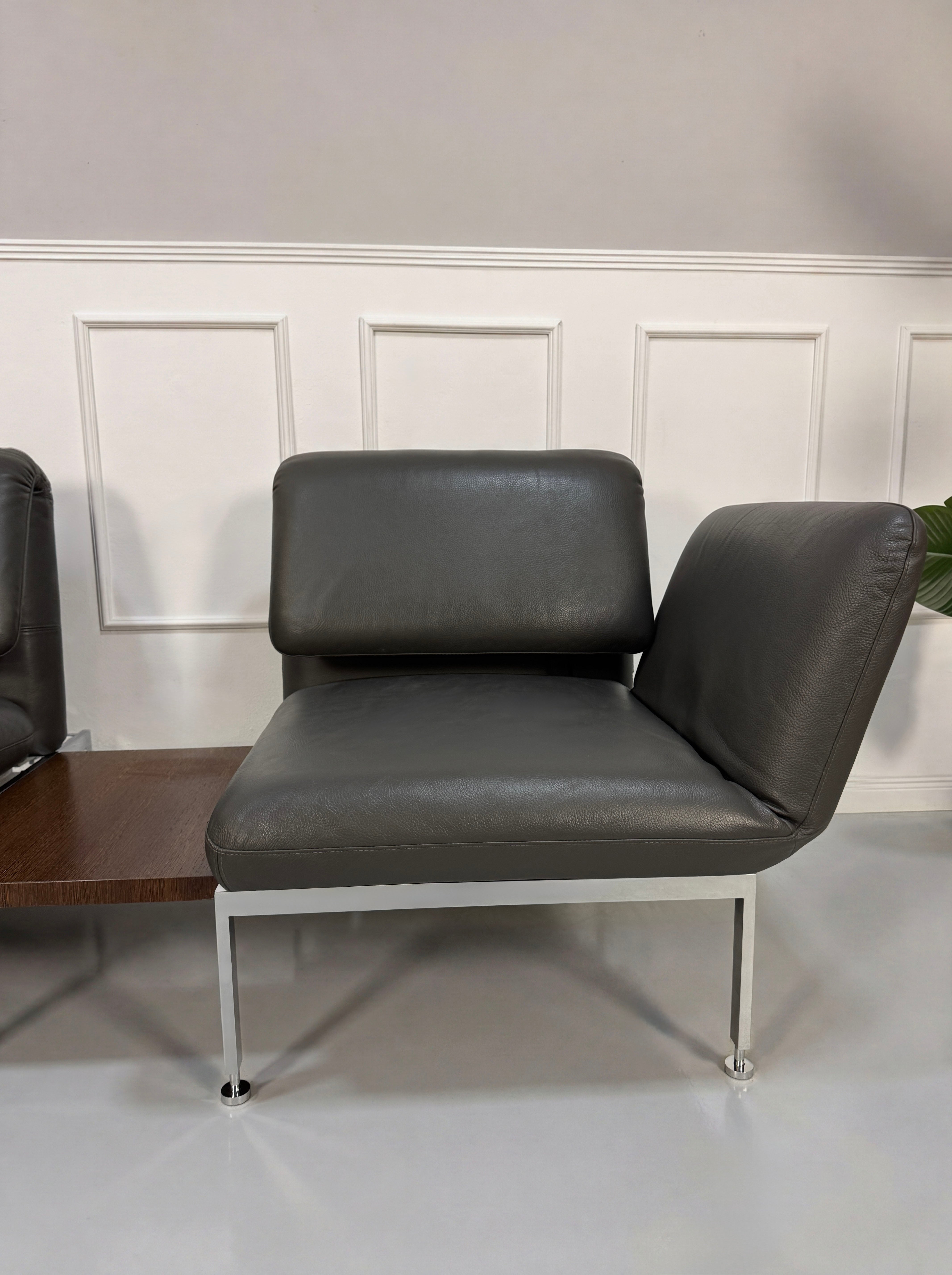 Gebrauchtes graues Brühl Roro Designer Leder Sofa mit Tisch vor einer Wand, stilvoll und modern eingerichtet.