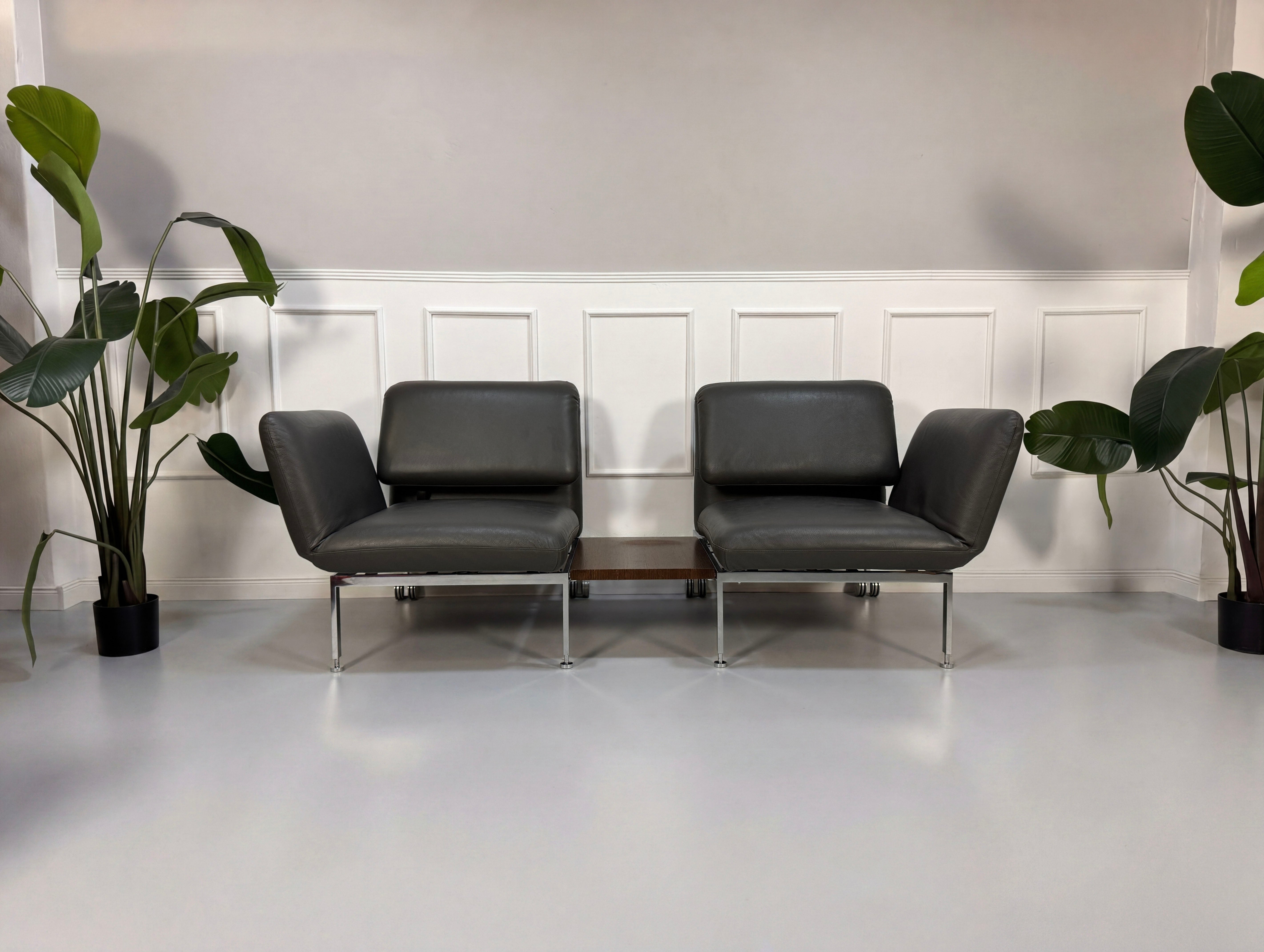 Gebrauchtes graues Brühl Roro Designer Leder Sofa mit Tisch vor einer Wand, stilvoll und modern eingerichtet.