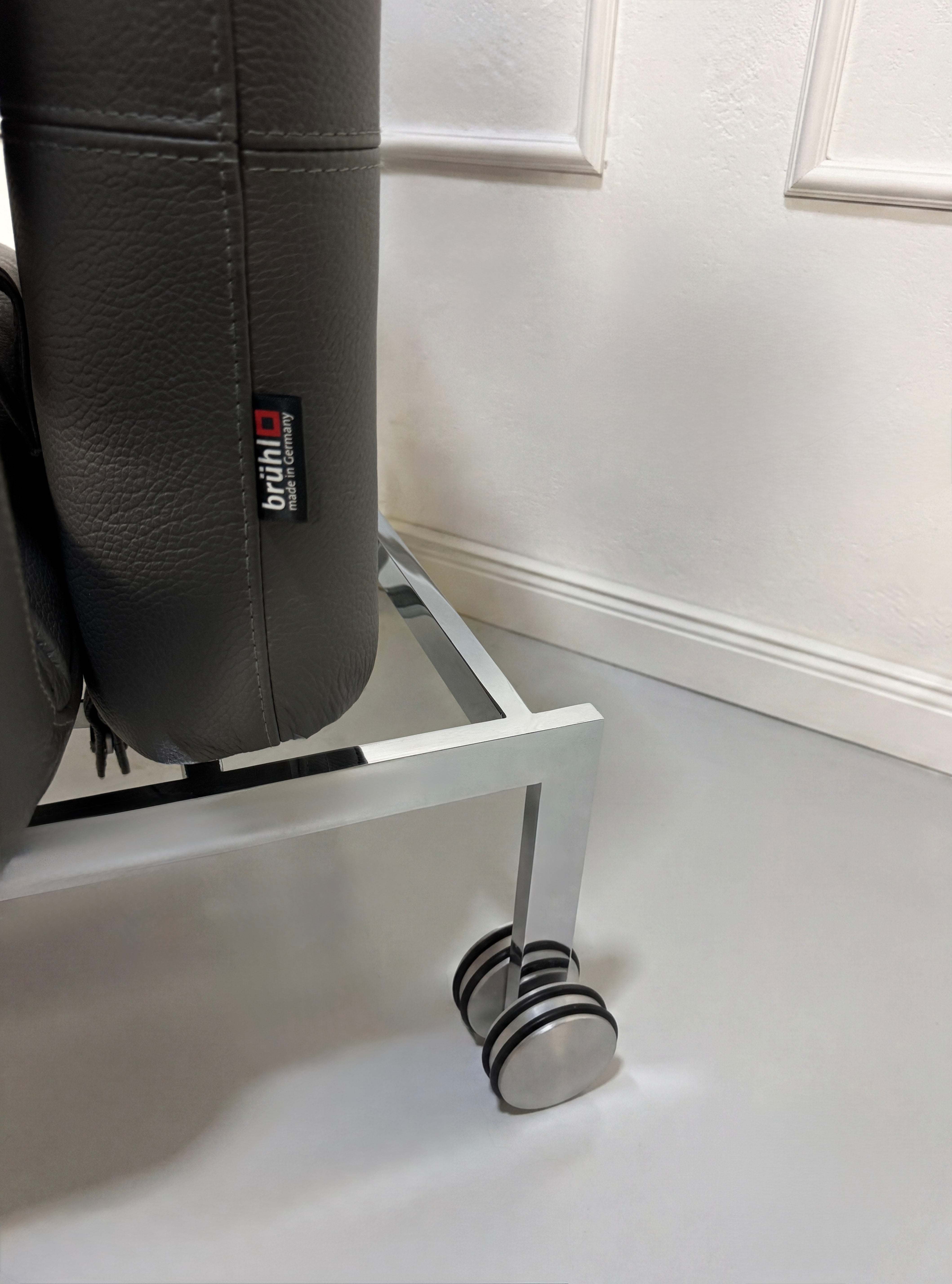 Gebrauchtes graues Brühl Roro Designer Leder Sofa mit Tisch vor einer Wand, stilvoll und modern eingerichtet.