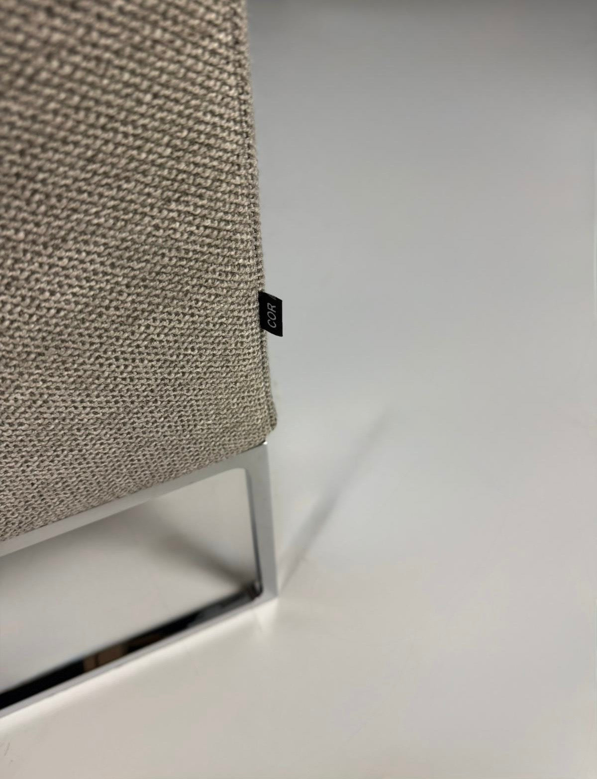 Gebrauchtes graues COR Mell Lounge Designer Stoff Sofa vor einer Wand, stilvoll und modern eingerichtet.