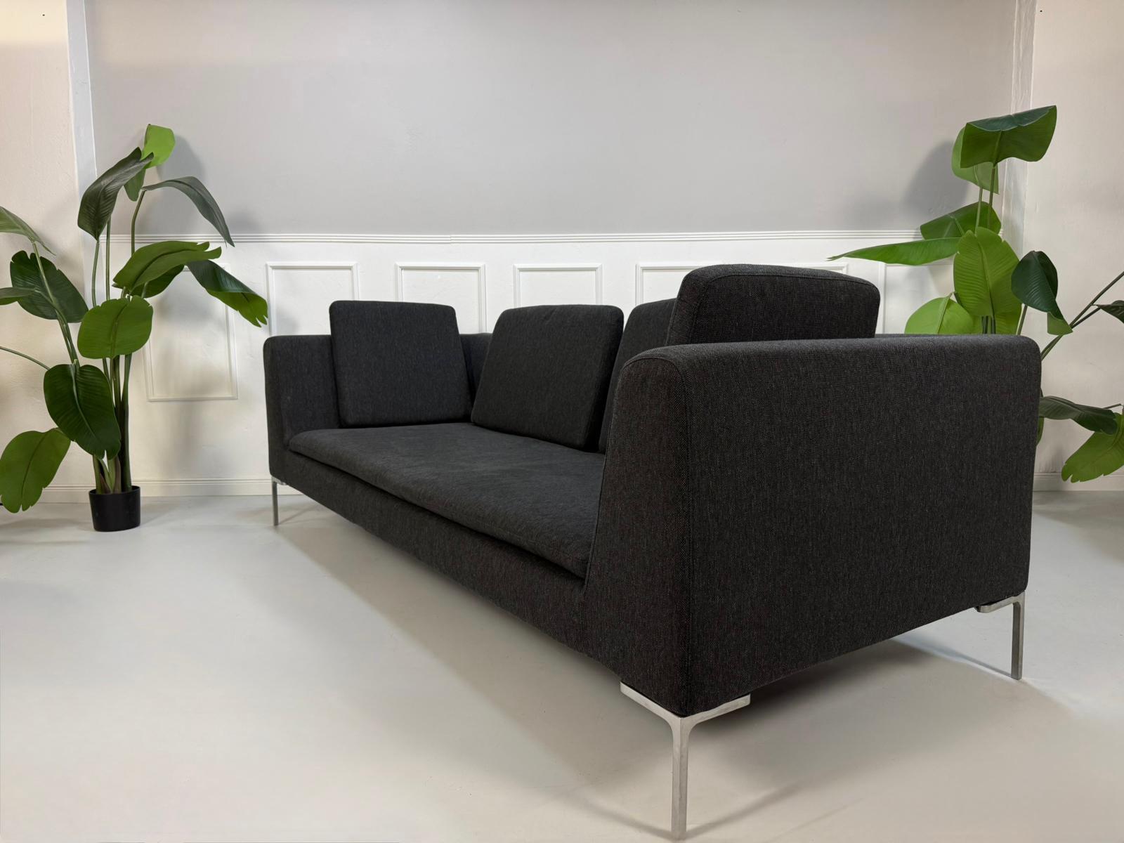 Refurbished graues B&B Italia Charles Designer Stoff Sofa vor einer Wand, stilvoll und modern eingerichtet.
