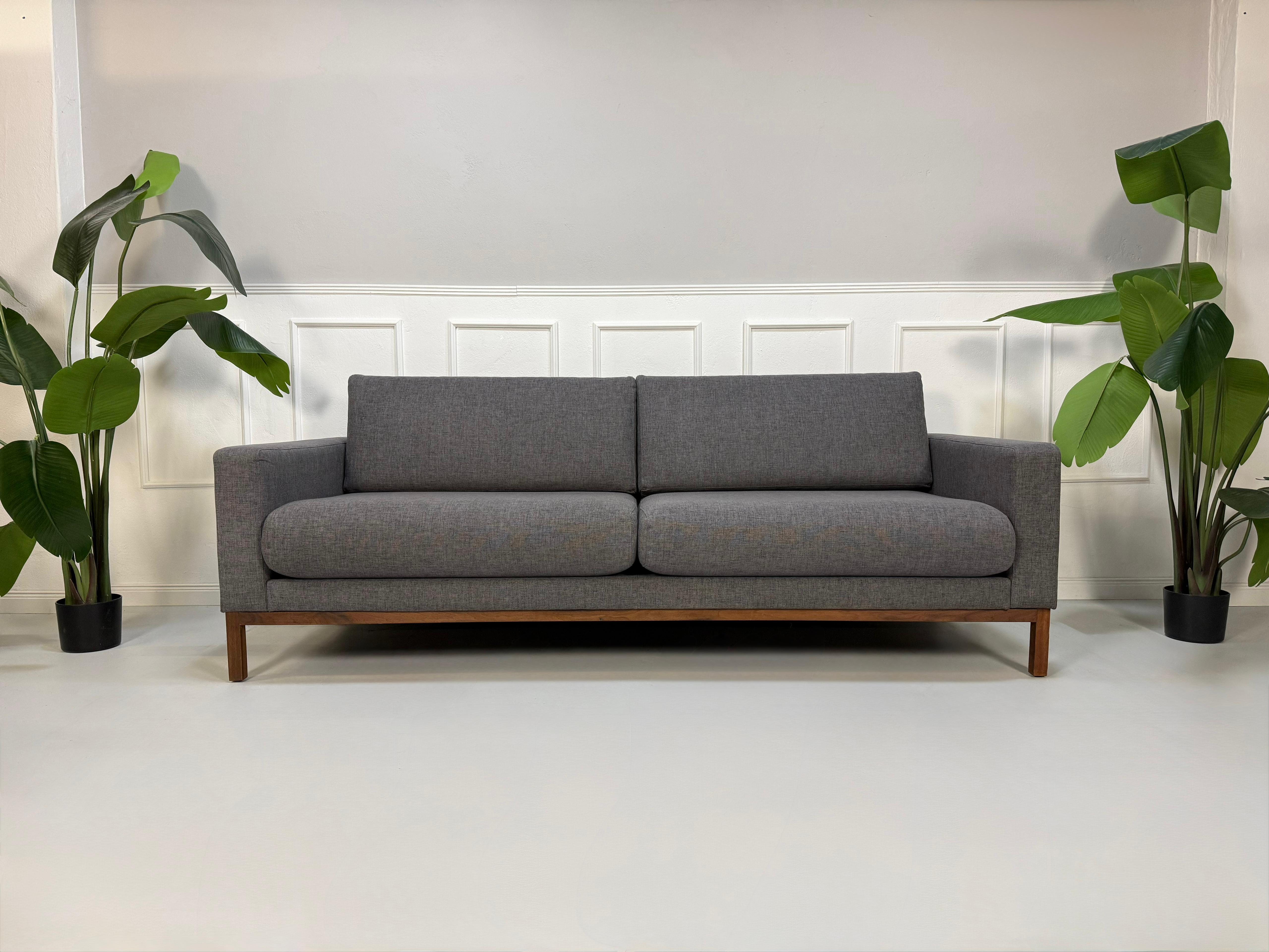 Gebrauchtes graues Bolia North Designer Stoff Sofa vor einer Wand, stilvoll und modern eingerichtet.