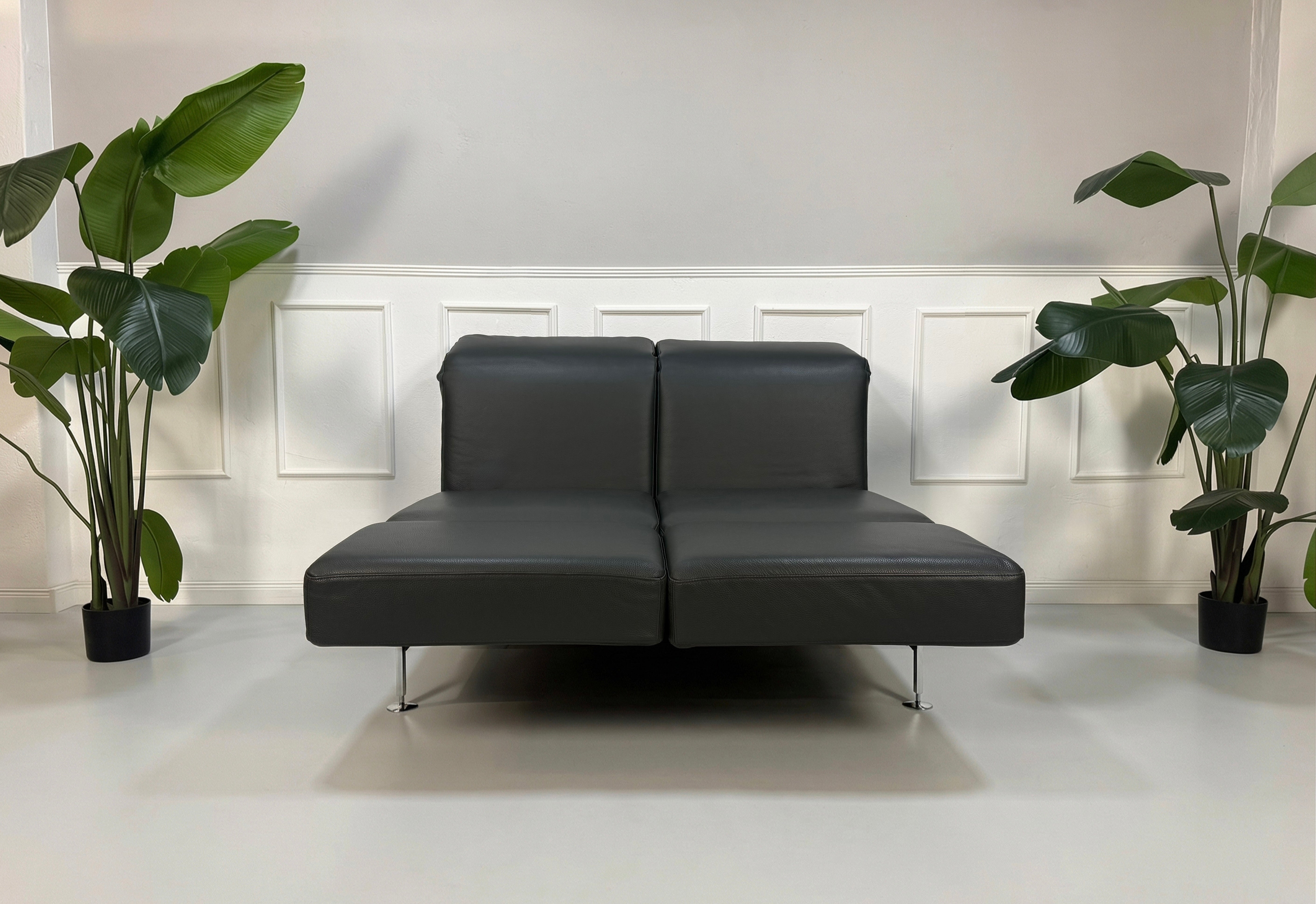 Gebrauchtes graues Brühl Moule Small Designer Leder Sofa vor einer Wand, stilvoll und modern eingerichtet.