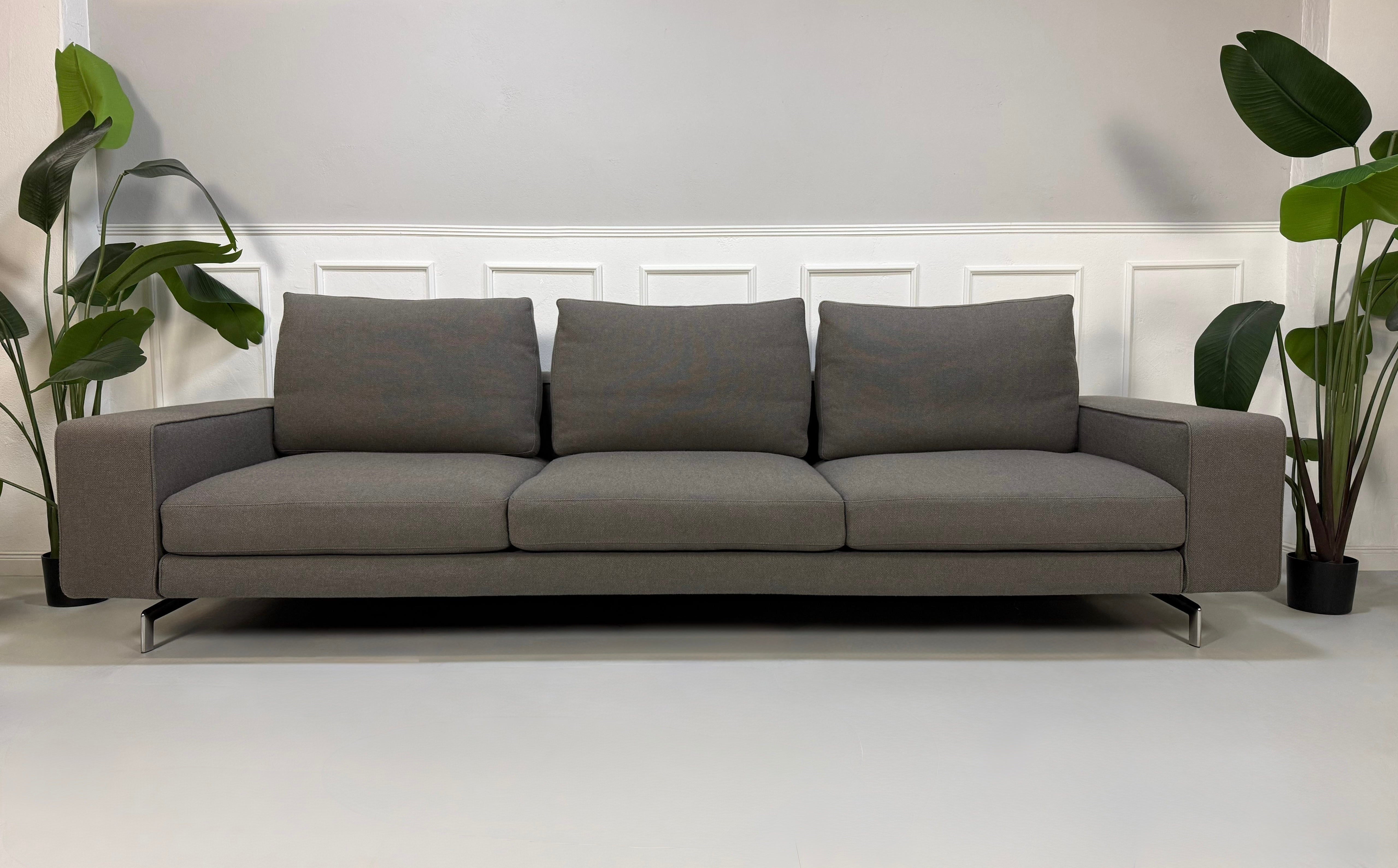 Erneuertes graues Minotti Sherman  Designer Stoff Sofa vor einer Wand, stilvoll und modern eingerichtet.