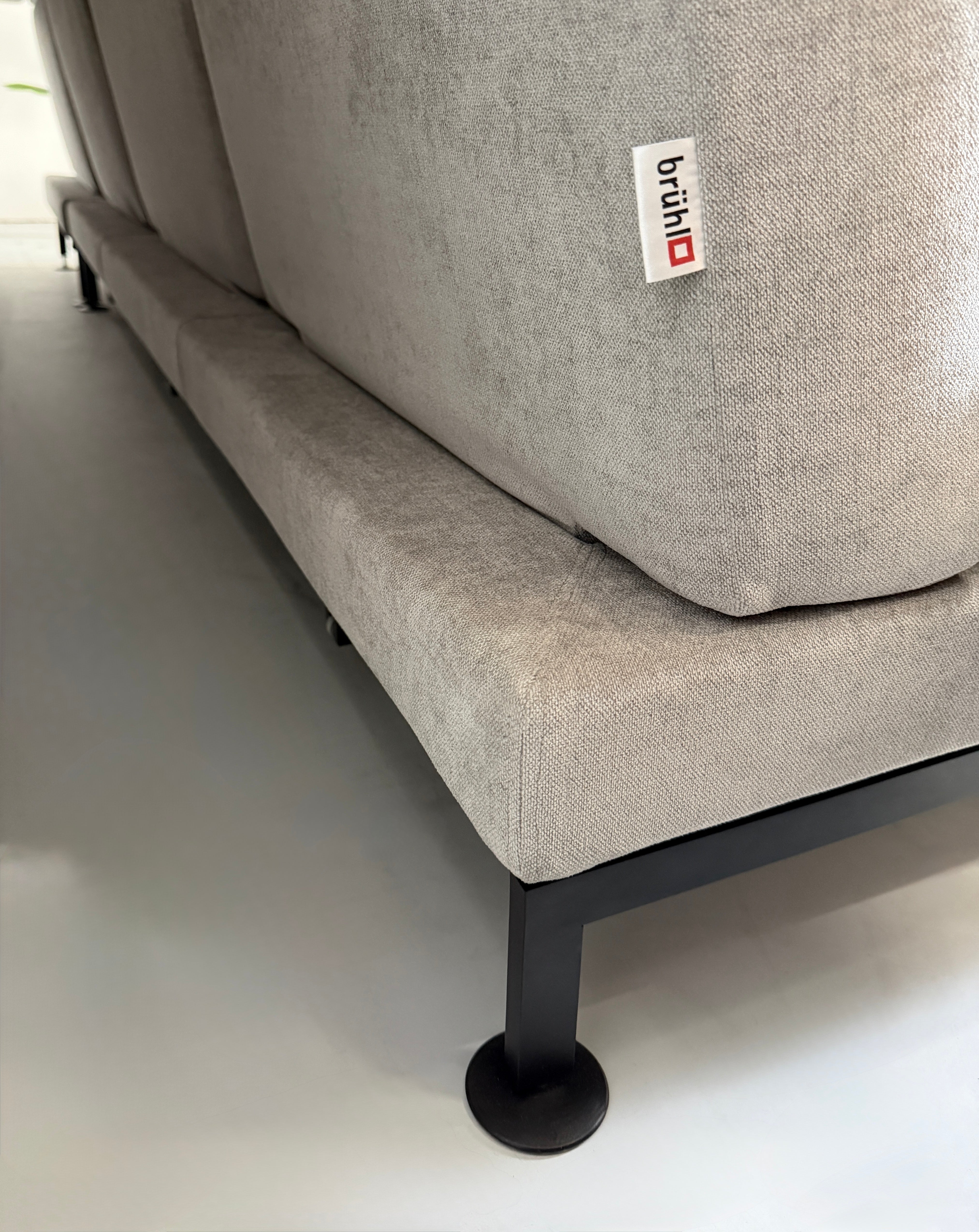 Graues Ausstellungsstück Brühl Moule Designer Stoff Sofa vor einer Wand, stilvoll und modern eingerichtet.